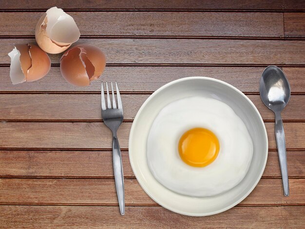 Photo spoon fork fried egg on plate on a wooden floor background