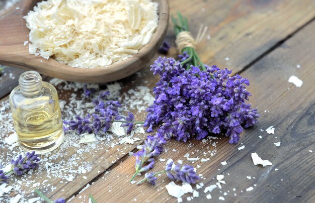 Spoon full of flakes of soap with essential oil and bunch of lavender flowers on wooden background