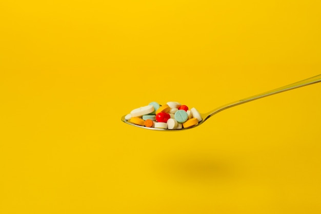 黄色の背景に丸薬でいっぱいのスプーン。セルフメディケーションと薬物乱用の概念。