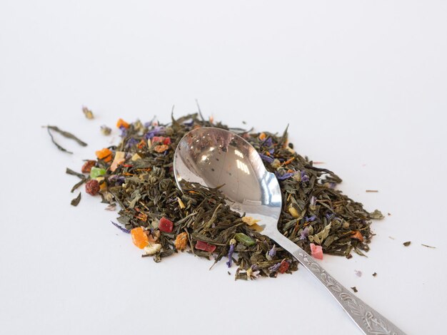 Spoon and green tea with fruit pieces and herbal leaves scattered on white