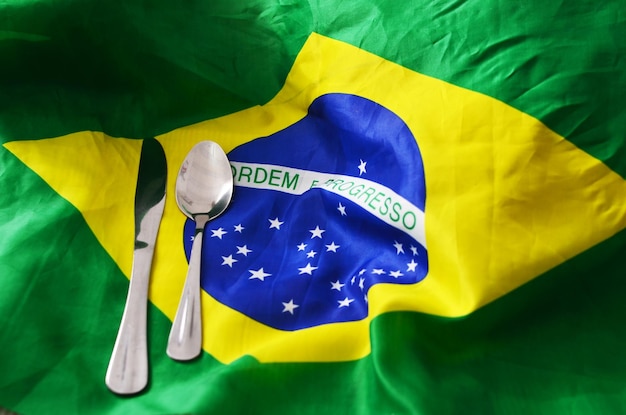 ブラジル国旗の上にスプーンとナイフ。政治、政府、飢餓の概念。