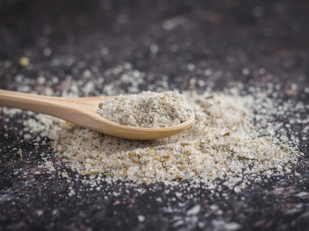 Spoon light wood on the pile of salt with herbs on a wooden table.