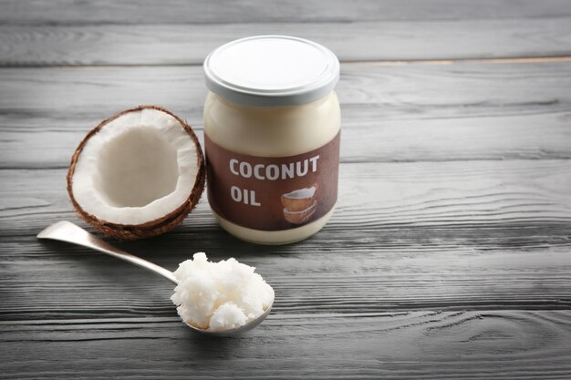 Spoon near glass jar with fresh coconut oil on grey wooden background