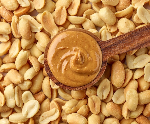 Spoon of peanut butter on peanut background, top view