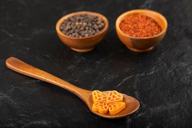 Spoon of raw pasta and pepper spices on black background. 