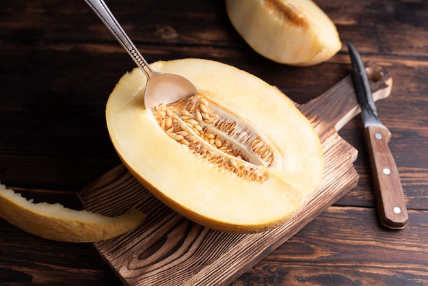 Photo spoon in the seeds of half a ripe melon on a cutting board on a dark wooden background.