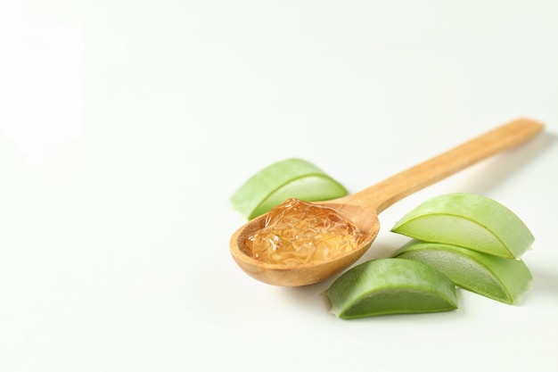 Spoon with aloe gel and slices on white background