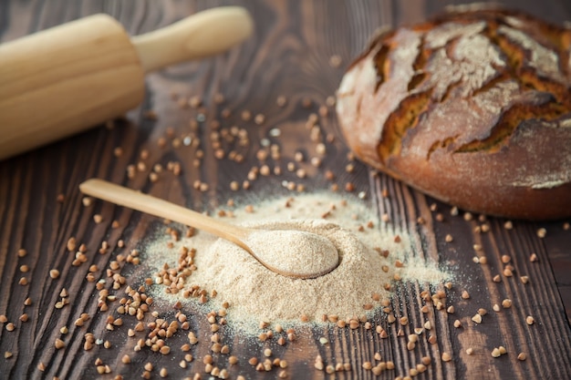 Spoon with buckwheat flour and a bread on a wooden background. Alternative flour. Gluten free and healthy eating.