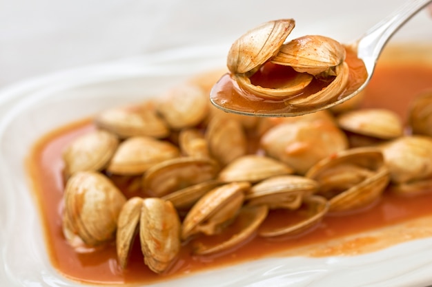 Spoon with clams in sauce on a plate of clams.