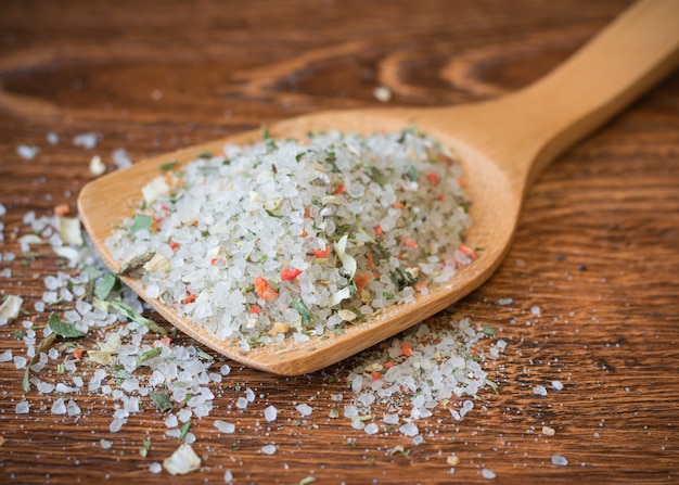 Photo spoon with coarse sea salt and spices on a wooden table.