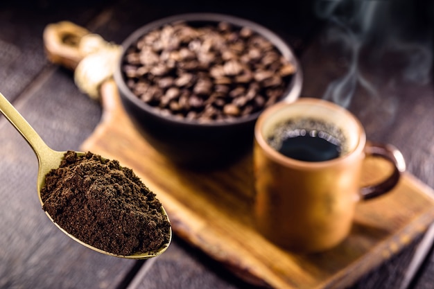 Spoon with coffee powder and cup with hot coffee in the background, spot focus