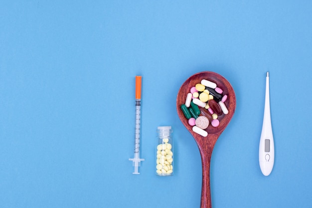 Spoon with colorful tablets and syringe and thermometer.