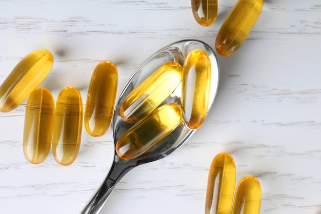 Spoon with fish oil capsules on white wooden background