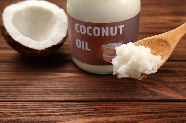Spoon with fresh coconut oil taken from glass jar on wooden background