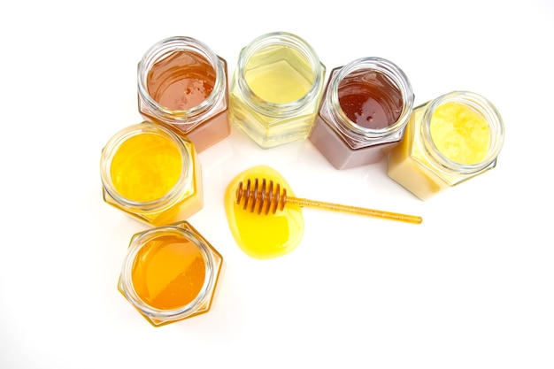 Ложка свежего меда и банки с разными видами меда на белом фоне. органические витаминные продукты