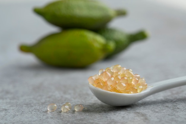 Spoon with fresh raw finger lime caviar close up and whole fruits at the background