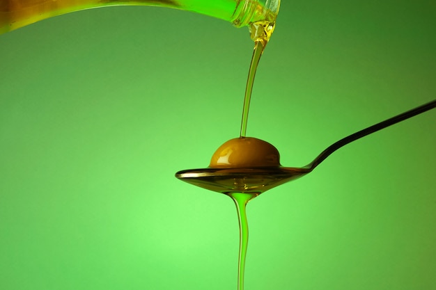 A spoon with an olive under a fall of oil on green background