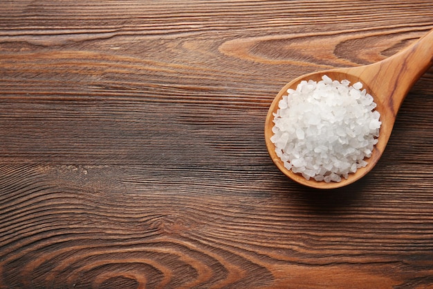 Spoon with sea salt on wooden background