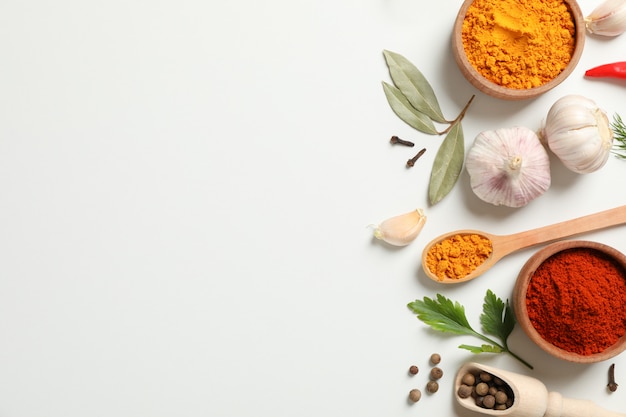 Spoons and bowls with different spices and ingredients on white, space for text