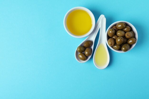 Spoons and bowls with olives and oil on blue