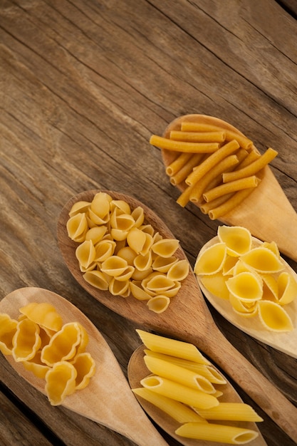 Spoons filled with varieties of pasta on wooden surface