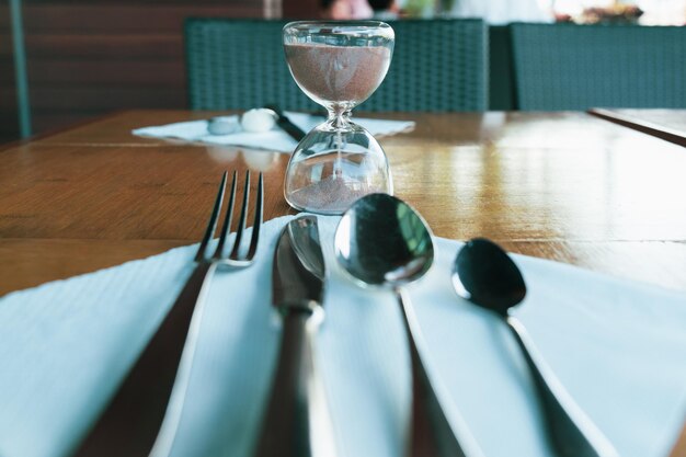 Foto cucchiai forchette coltelli e orologi a sabbia sul tavolo da pranzo concetto di tempo per mangiare