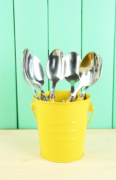 Spoons in metal bucket on color wooden background