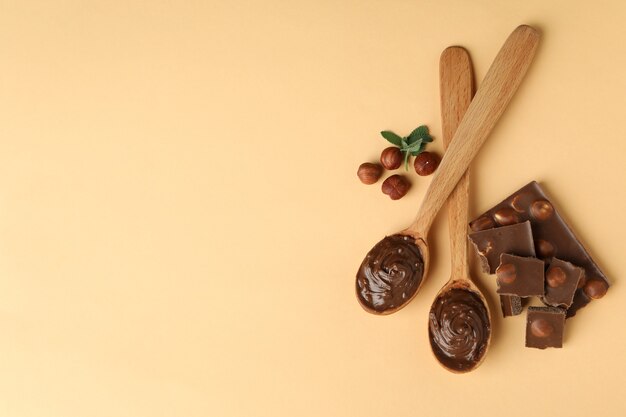 Spoons with chocolate paste, nuts, chocolate and mint on beige background