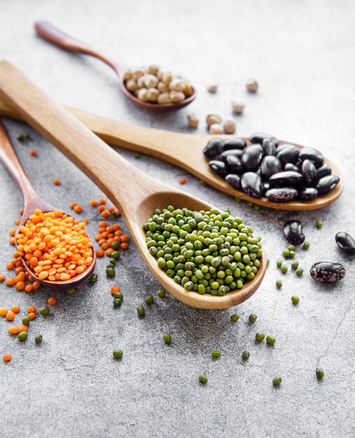 Spoons with different types of legumes on a gray concrete surface