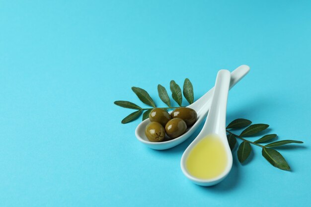 Spoons with olives and oil, and twigs on blue surface