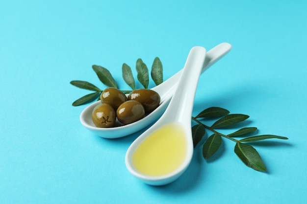 Spoons with olives and oil, and twigs on blue