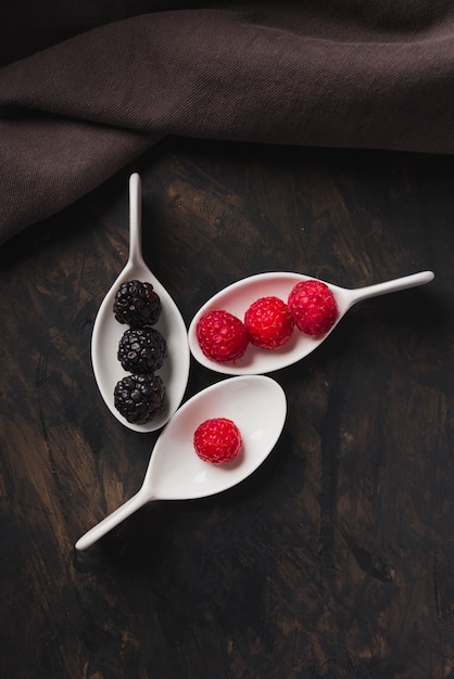 Spoons with raspberry and blackberries background black and cloth