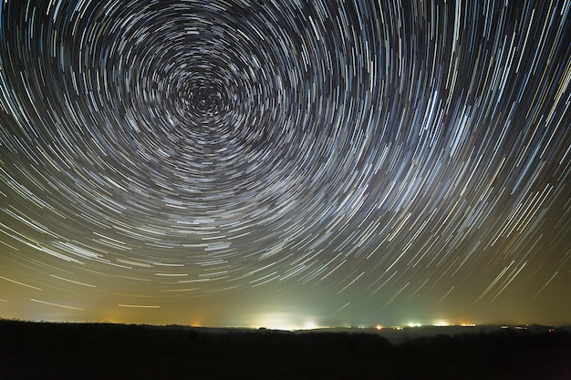 Spoor van sterren aan de nachtelijke hemel rond de Poolster. Gefotografeerd met een lange belichting van de verlichte stad.