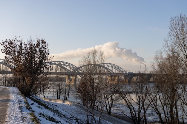 Spoorbrug over een winterrivier tegen de achtergrond van rokende schoorstenen