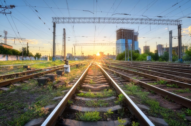 Spoorweg bij prachtige zonsondergang in Europa Industrieel landschap met treinstation groen gras gebouwen blauwe lucht met zon Spoorwegknooppunt in de avond Spoorwegplatform Vervoer