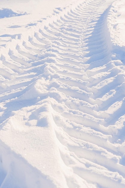Sporen van tractorwielen in de sneeuw. De afdruk van het loopvlak van de uitrusting van gemeentelijke diensten tijdens het sneeuwruimen. Verticale foto