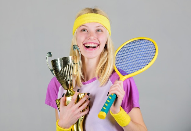 Sport achievement. Celebrate victory. Tennis champion. Athletic girl hold tennis racket and golden goblet. Win tennis game. Tennis player win championship. Woman wear sport outfit. First place.