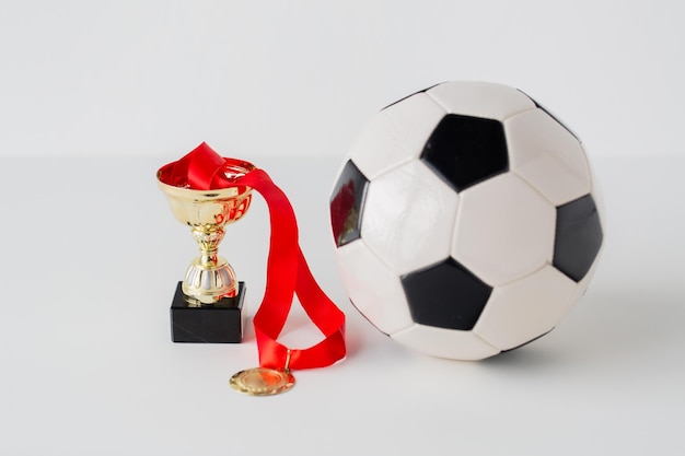 Foto concetto di sport, realizzazione, campionato, competizione e successo - primo piano del pallone da calcio o da calcio con medaglia d'oro e coppa su sfondo bianco