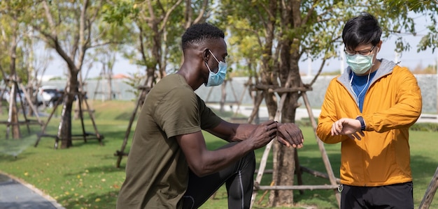 Sport Afro-Amerikaanse man en Aziatische man die prestaties of hartslagpulstrace controleert. Mensen dragen een chirurgisch gezichtsmasker tijdens de uitbraak van coronavirus en griep