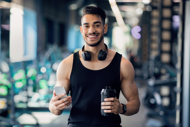 Sport app cheerful middle eastern male athlete posing with smartphone in hand