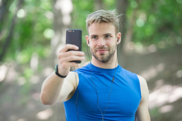 App per lo sport sul telefono. sport digitale. orologio intelligente. uomo atletico in abiti sportivi fa selfie. allenamento all'aperto. applicazione per il fitness. ui ux concetto. gadget nello sport moderno. uomo muscoloso in tracker. ricerca di connessione.