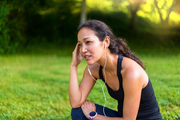 スポーツアジアの女性のヘッドフォンで音楽を聴くとトレーニングの後の残り