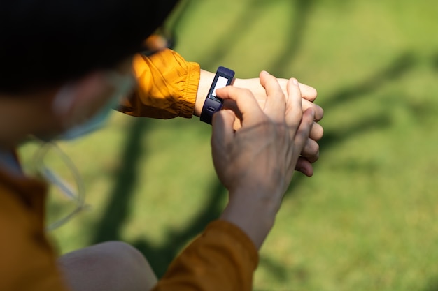 Sport Aziatische man die prestaties of hartslagpulstrace controleert. Sport en fitness buitenshuis. Mannelijke loper die op zoek is naar een slim sporthorloge. draag een chirurgisch gezichtsmasker tijdens de uitbraak van coronavirus en griep