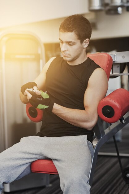 sport, bodybuilding, lifestyle, technology and people concept - young man with smartphone in gym