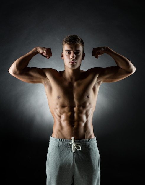 Photo sport, bodybuilding, strength and people concept - young man showing biceps over black background