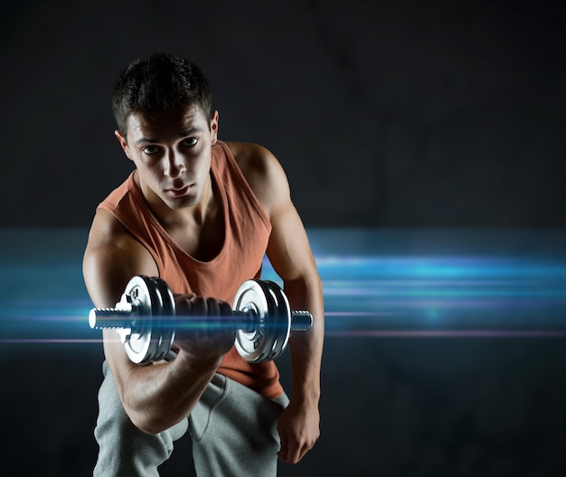 sport, bodybuilding, training and people concept - young man with dumbbell flexing biceps over dark background