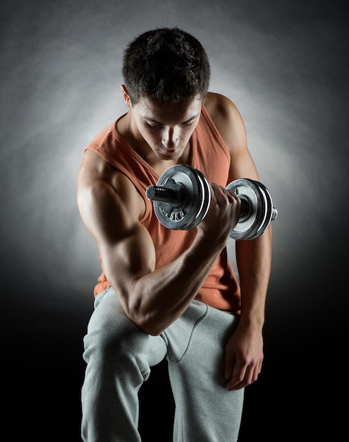 sport, bodybuilding, training and people concept - young man with dumbbell flexing muscles over gray background