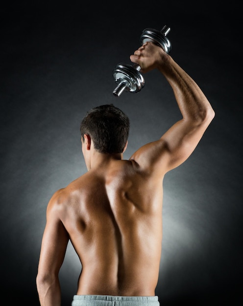 sport, bodybuilding, training and people concept - young man with dumbbell flexing muscles over gray background