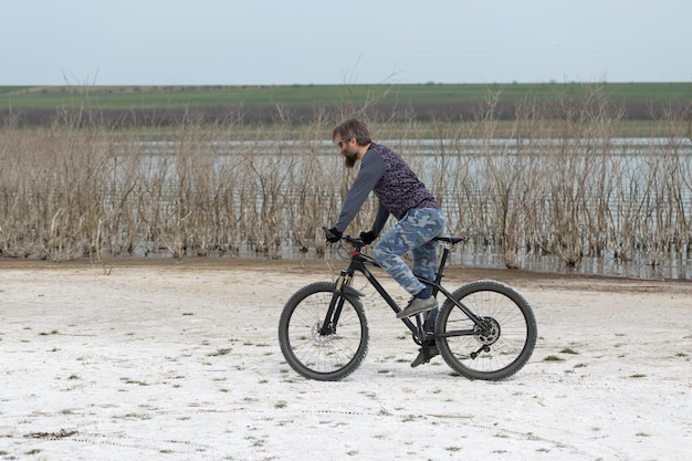 Sport brute bebaarde man op een moderne mountainbike Een fietser op een zout verlaten plek aan het meer