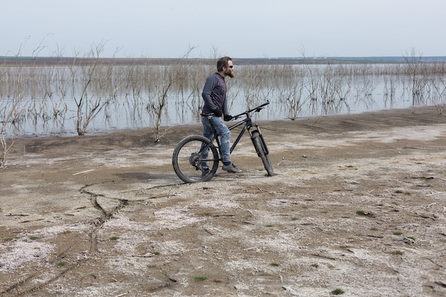 Sport brute bebaarde man op een moderne mountainbike. Een fietser op een zout verlaten plek aan het meer.